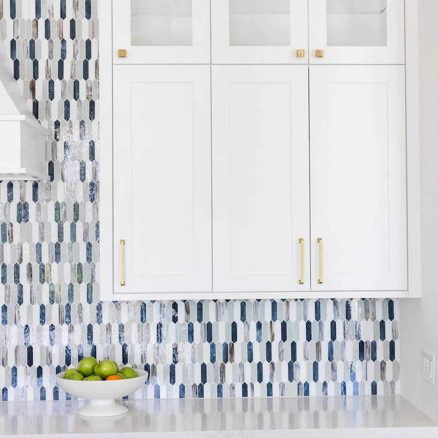 blue glass tile against white shaker cabinets and gold hardware