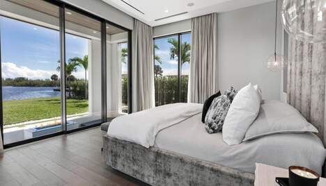 Large luxurious bed in modern home with a wide backyard and a lake.