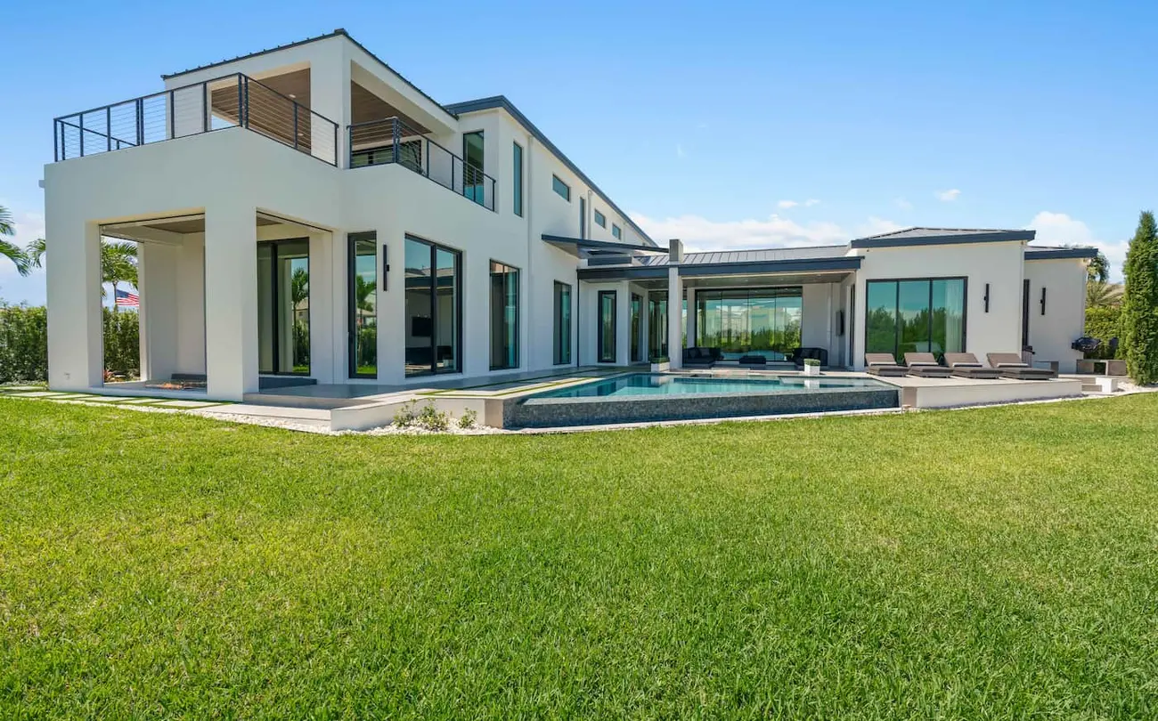 Large white house in modern design with a wide backyard and a pool.