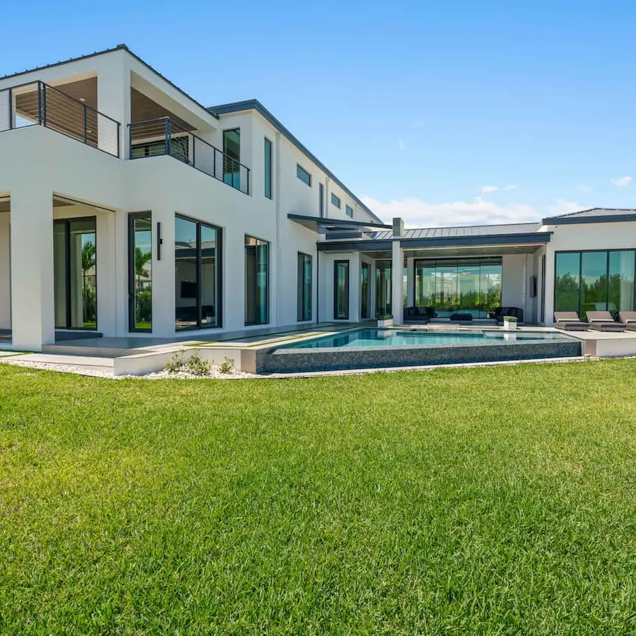 Large white house in modern design with a wide backyard and a pool.