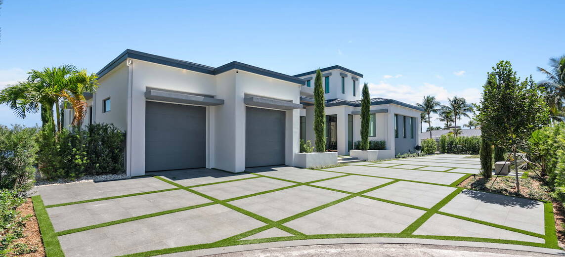 A large driveway with a white modern house and a two car garage.