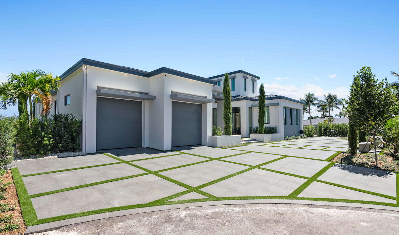 A large driveway with a white modern house and a two car garage.