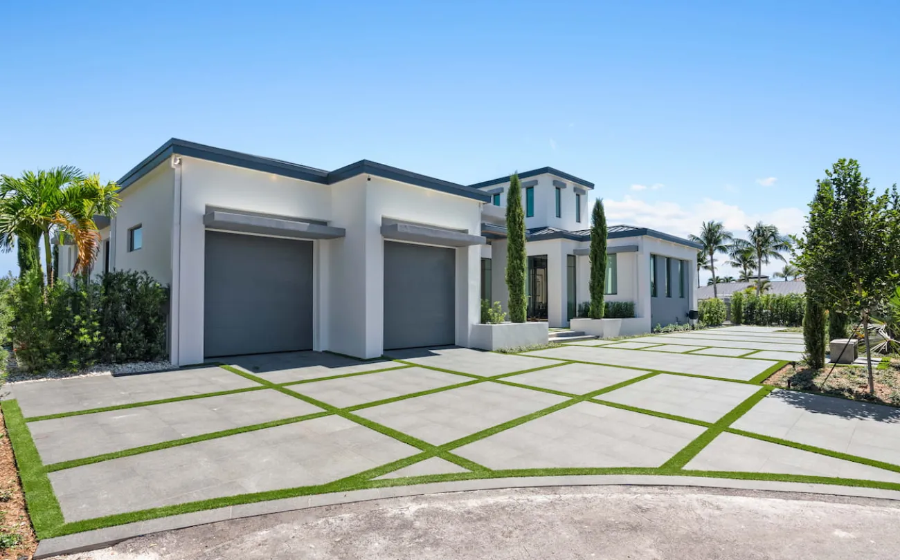 A large driveway with a white modern house and a two car garage.
