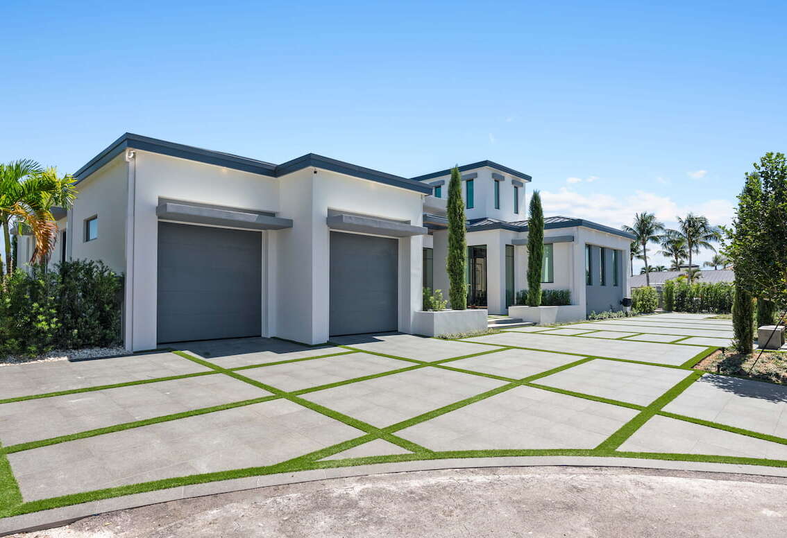 A large driveway with a white modern house and a two car garage.