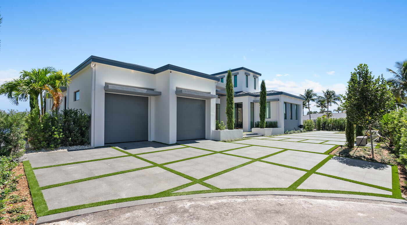 A large driveway with a white modern house and a two car garage.