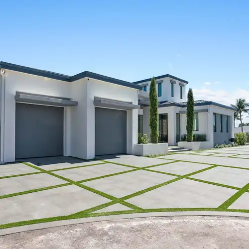 A large driveway with a white modern house and a two car garage.