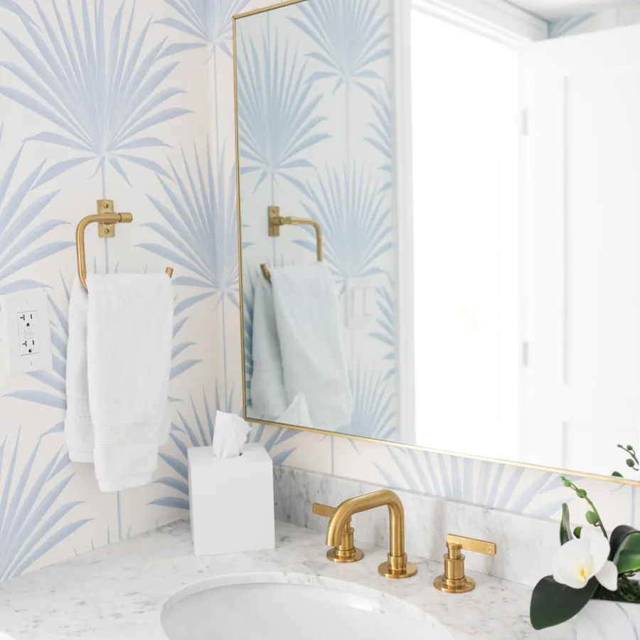 Elegant bathroom with brass fixtures and palm wallpaper.