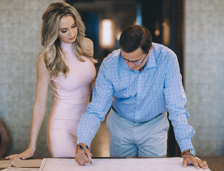 Don Rothrock at a desk marking up blue prints as a woman is beside him.